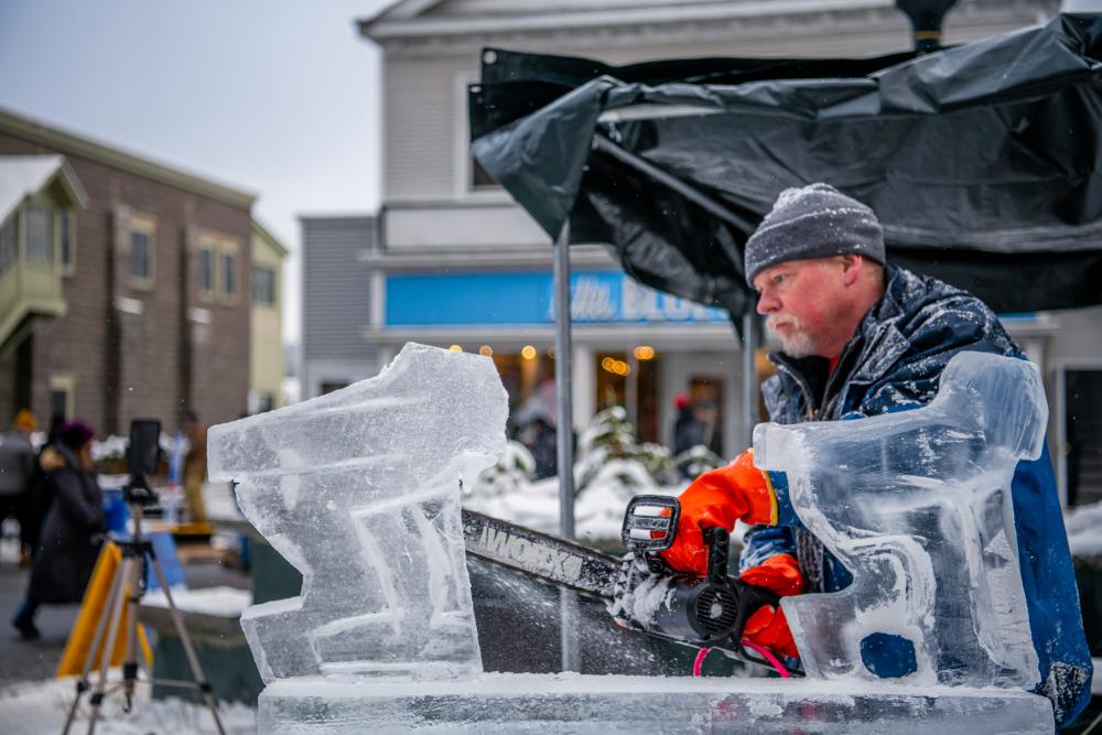 A man holding a chainsaw carves a sculpture out of ice.