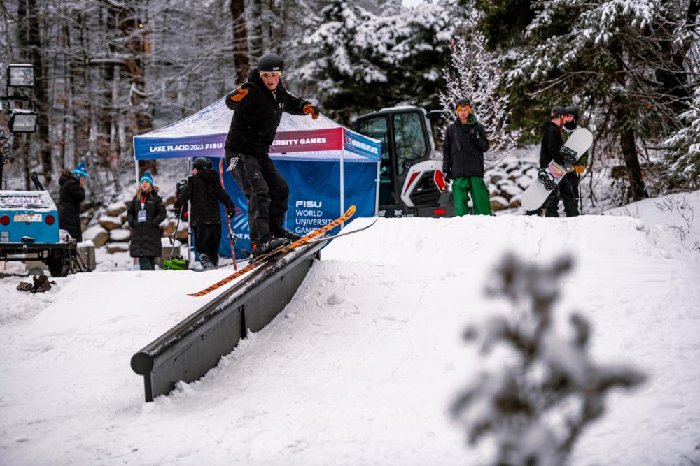 A snowboarder rides down a railing on a snowy bank.