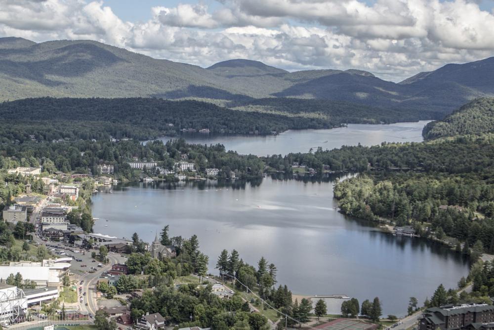 An aerial view of the village of Lake Placid, lined with shops and restaurants, and adjacent to Lake Placid lake and Mirror Lake.