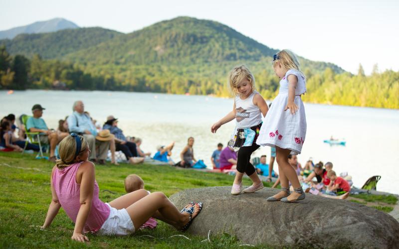 Kids dance on a rock in Mid's Park with Mirror Lake and the mountains in the backdrop