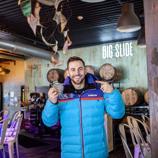 An Olympian holding up a bronze medal in a brewery