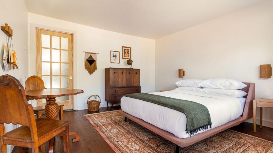 a rustic style bed in a hotel room with wood table and chairs. 