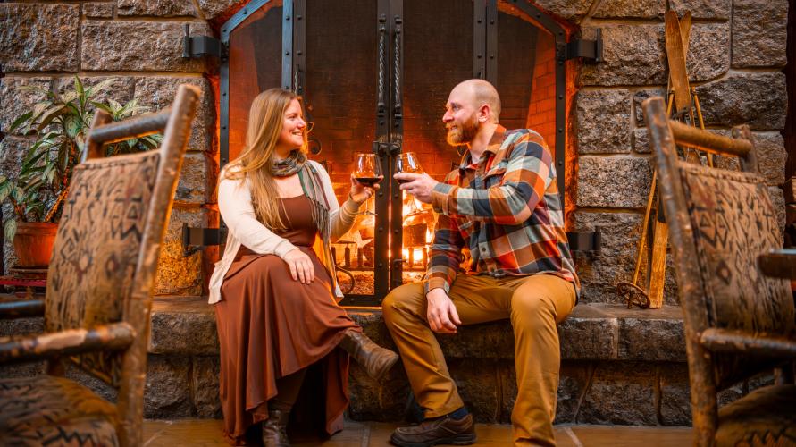 Man and woman cheers red wine in front of fireplace