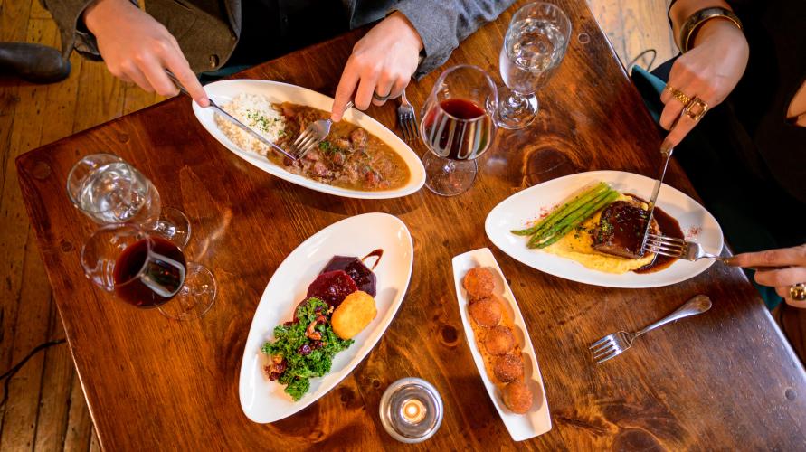 Multiple plates on table with hands holding silverware 