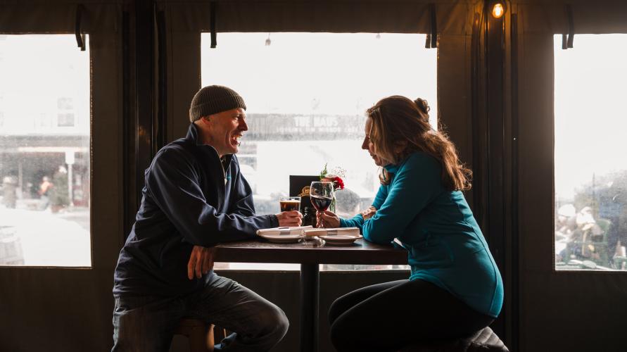 A couple sitting at a table in a restaurant, looking at each other and smiling.