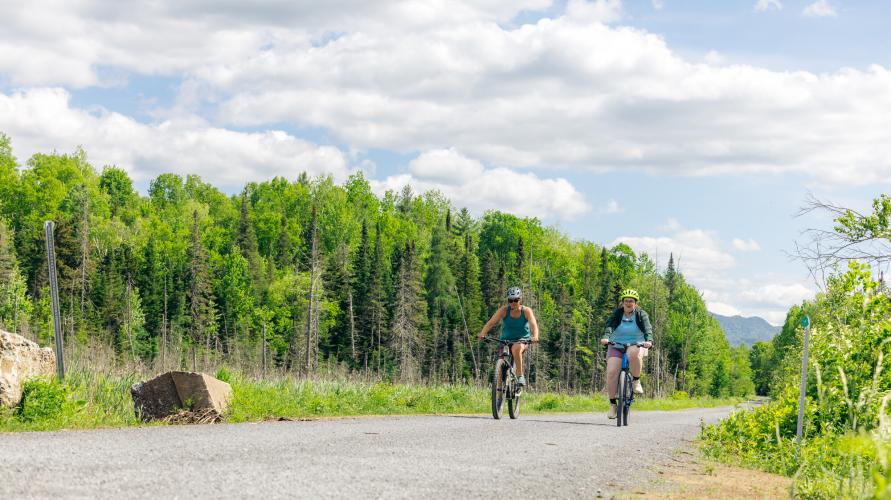 Two women ride bikes on a wide gravel trail 