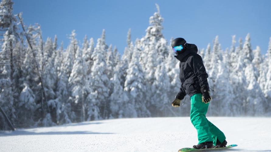 A snowboarder in black jacket and green pants rides down a snow-laden mountain.