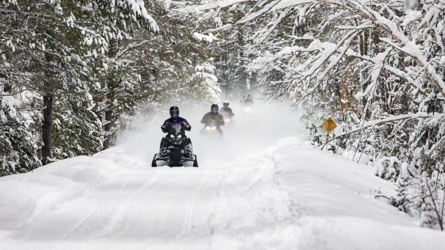 Snowmobilers riding down the Adirondack Rail Trail in the winter.