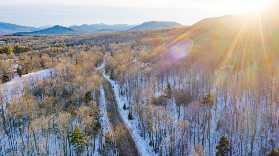 An aerial view of a snowy landscape and scenic road with mountains in the background.