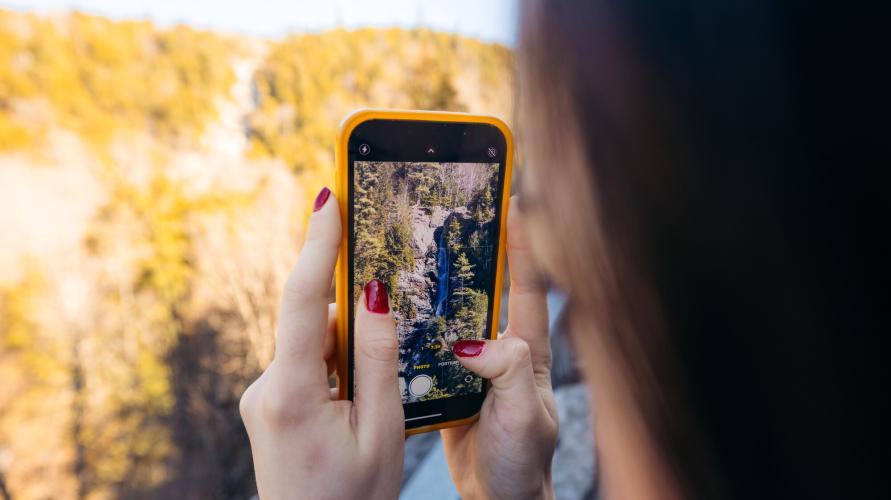 A woman takes a photo of a waterfall.