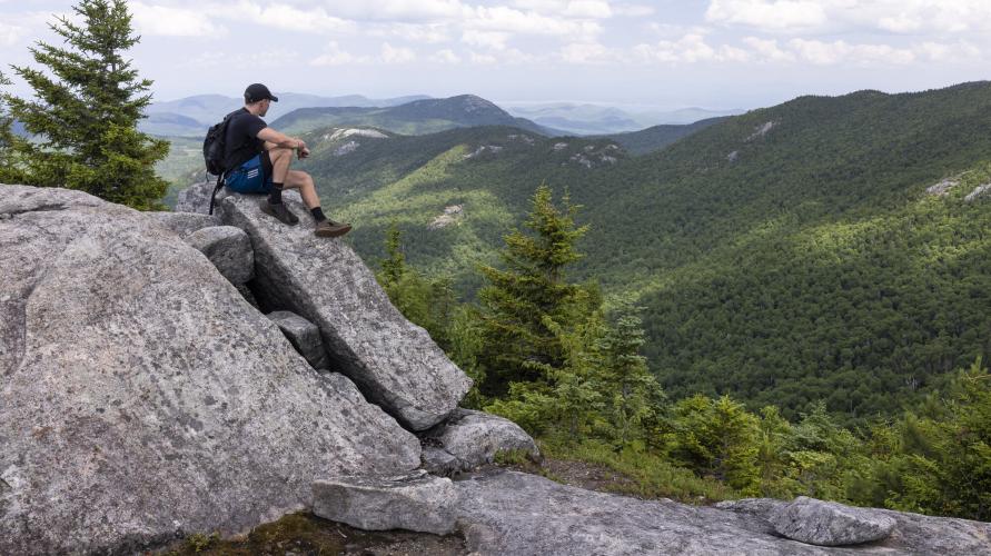 A man sitting on top of a rock looking out at the views on a hike.