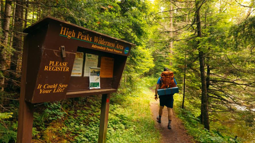 A hiker walking past a trailhead sign in.