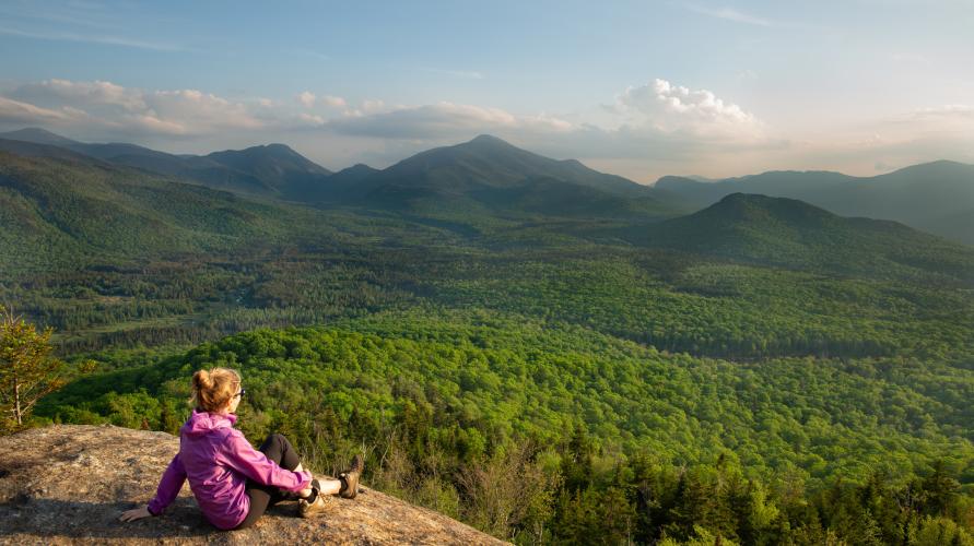 A woman sitting at the summit of a summer hike.