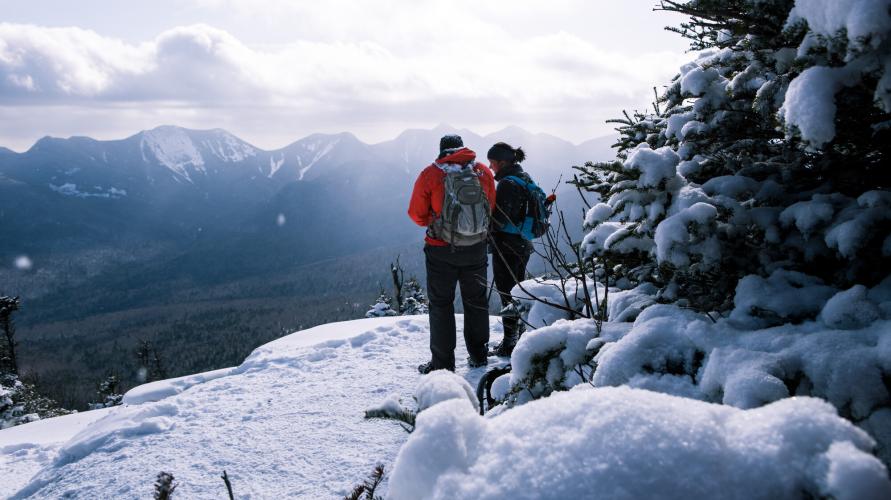 Two people standing at the summit of a mountain while on a winter hike.