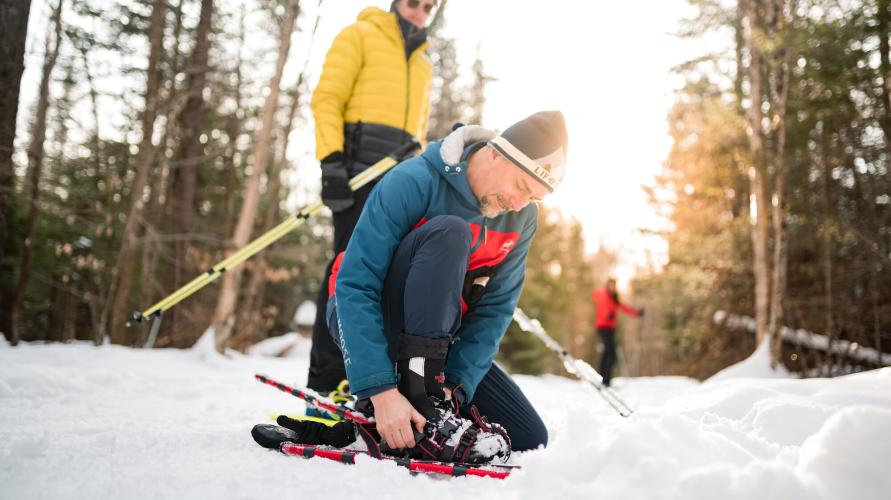 A group of snowshoers putting on their snowshoes in a snowy forest.