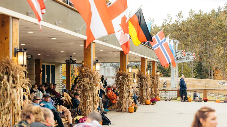 The patio of an Olympic venue is decorated with international flags, pumpkins, and dried corn stalks for fall.