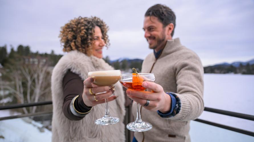 A man and a woman cheers their drinks outside on the deck of Top of the Park in Lake Placid.