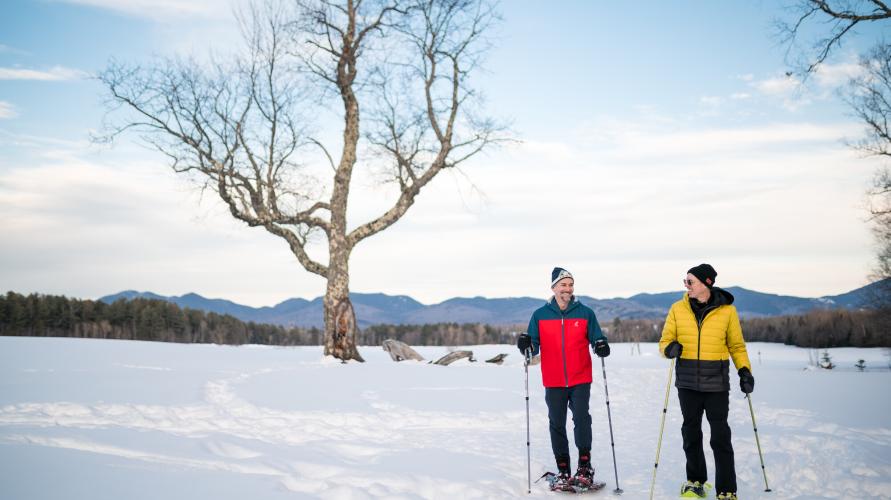 Two people snowshoeing with a snowy landscape behind them.