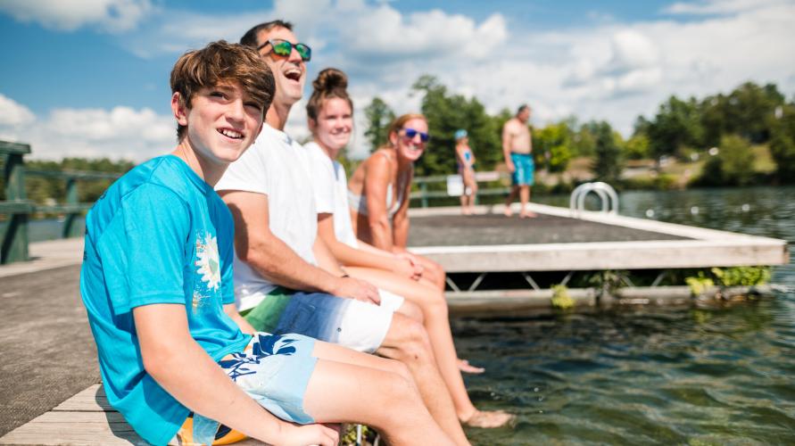 A family of four sits on a dock in summer.