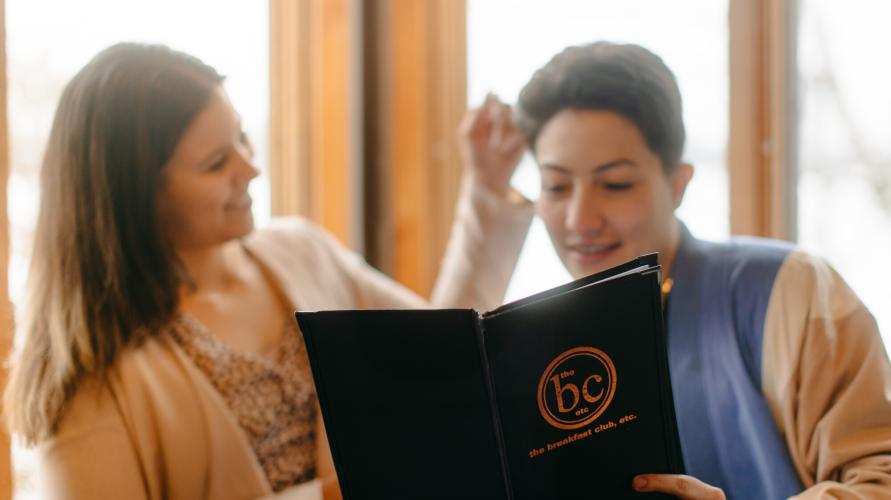 Two women smile at one another over a meal and mimosas