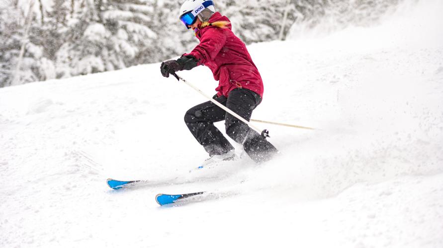 A woman skis in a red jacket and black ski pants. 