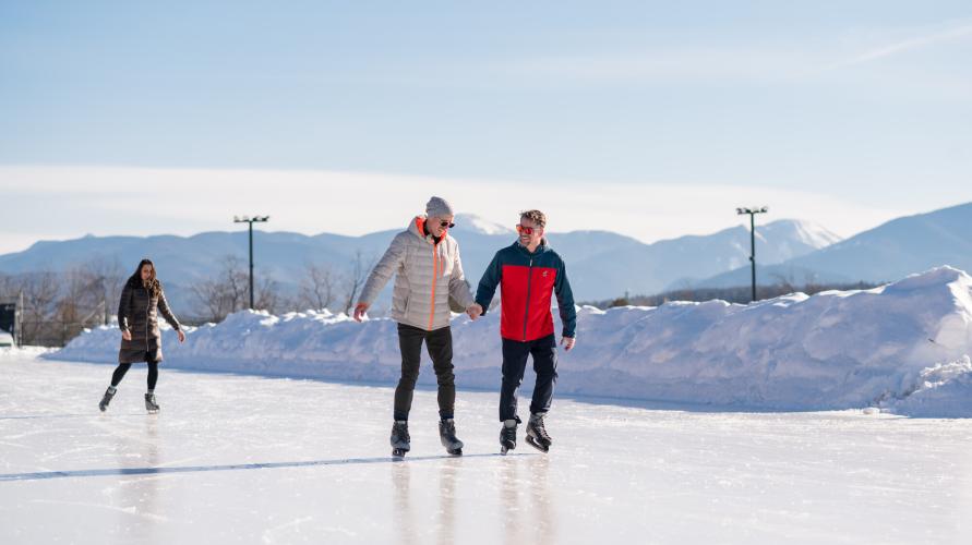 Two men hold hands while ice skating on an outdoor rink 