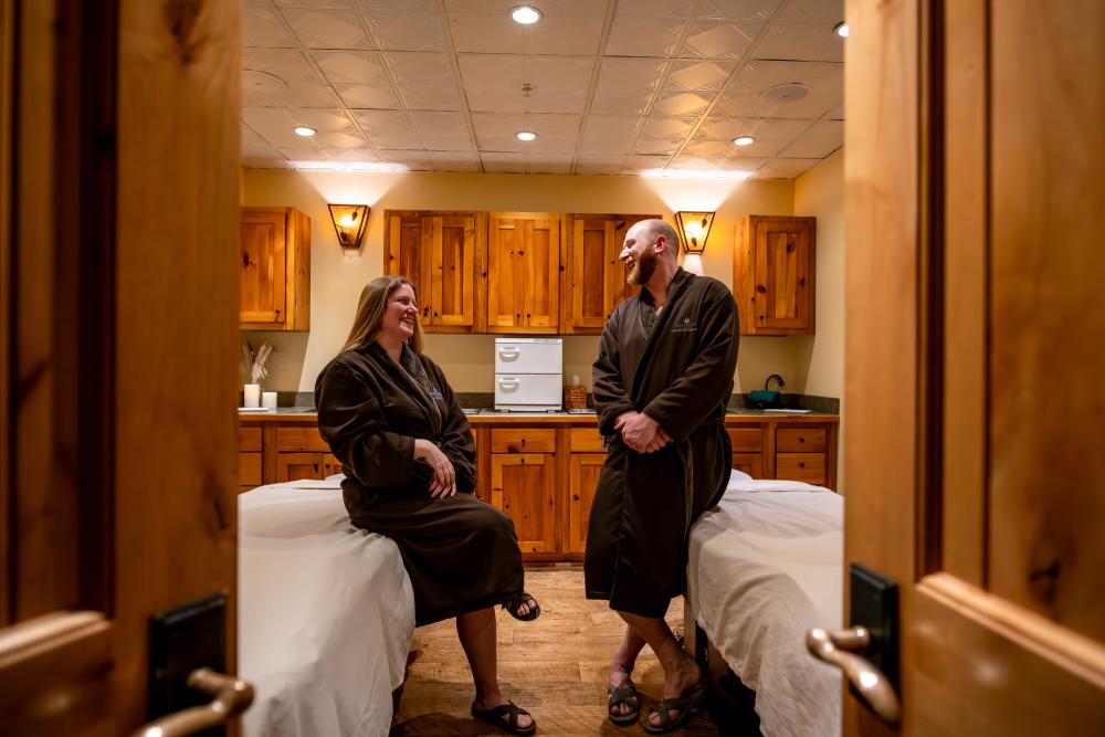 A man and woman laugh in spa robes before their massage.