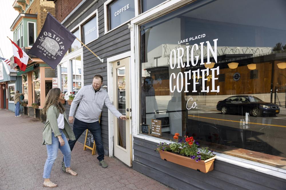 Man opening door of Origin Coffee shop looking back at woman