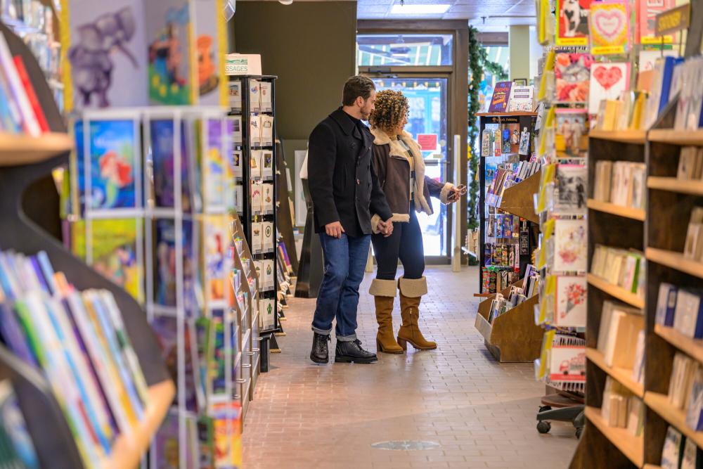 Couple wearing coats seen down the aisle of bookstore looking at books