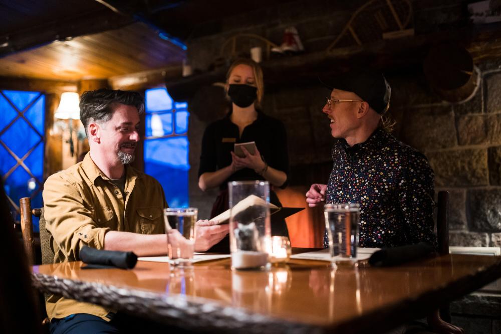 Two men sit in a cozy, dimly-lit rustic dining room at a luxury resort.