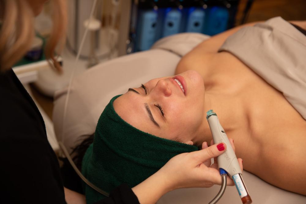 A close-up of a woman with her hair wrapped in a towel, eyes closed, receiving a relaxing spa treatment.