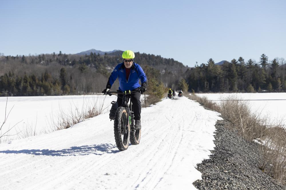 A man riding a fat tire bike over a thin snow trail.