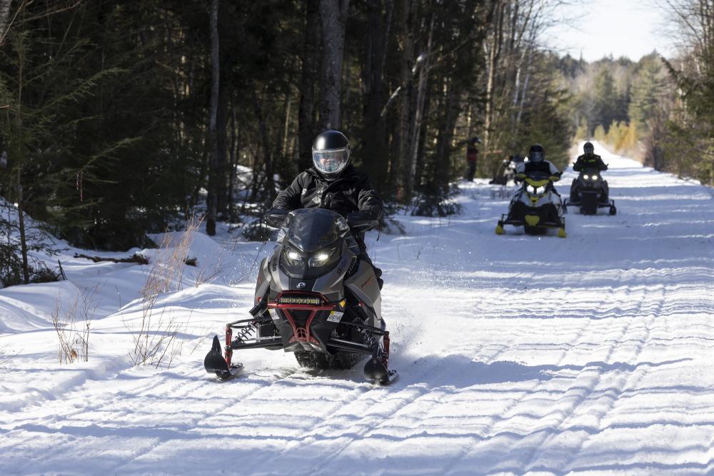 A group of snowmobilers ride along a snowy trail.