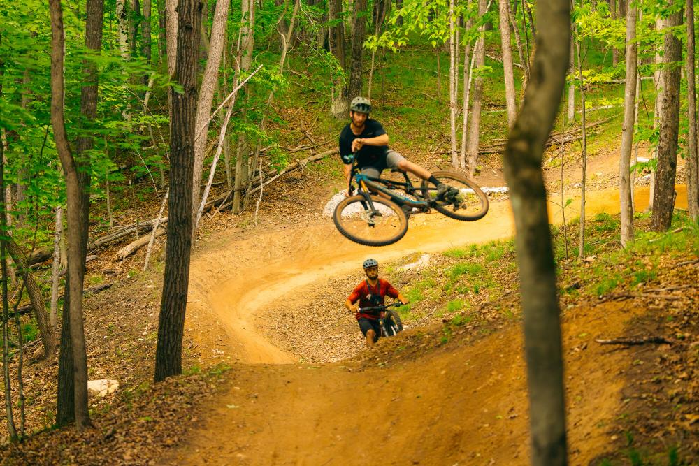 A mountain biker flies through the air off a jump in the woods.