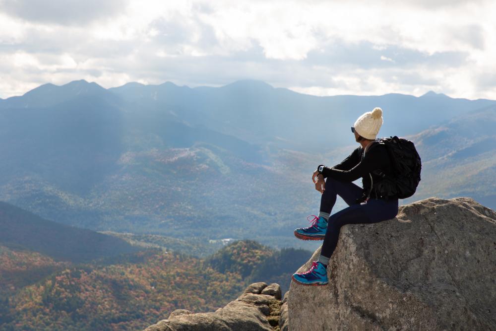 A woman sitting on a rock at the summit of a hike overlooking the mountains.