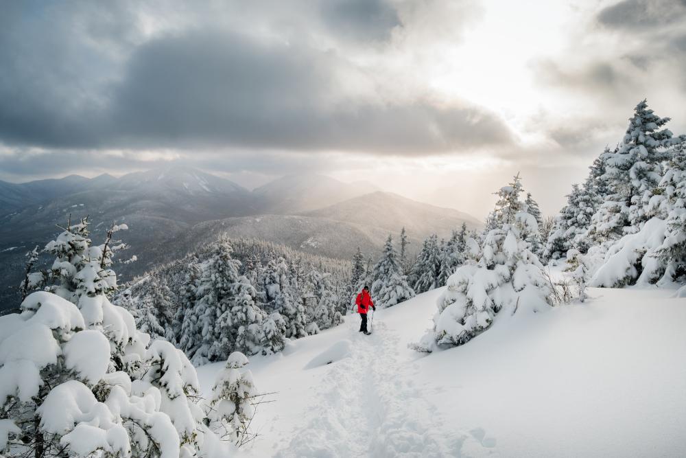 A person snowshoeing up a mountain in Keene during the winter with stunning mountain views in the background.