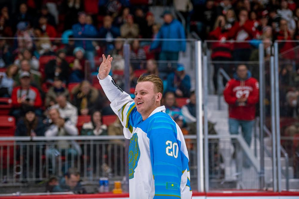 A male hockey player in uniform waves to fans from the ice.