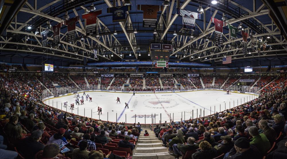 A wide-angle view of a hockey arena. Fans fill the stands and watch a game.