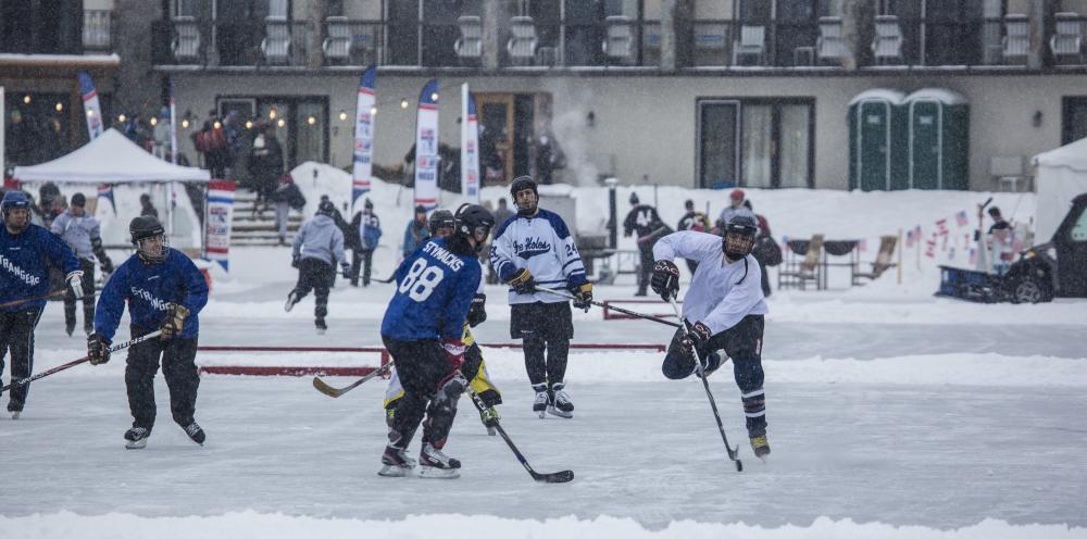 Pond hockey players compete on a snowy day at an outdoor rink.