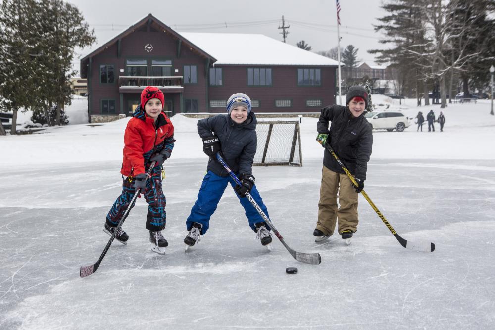 Three small boys pose with their sticks and a puck at lake rink.