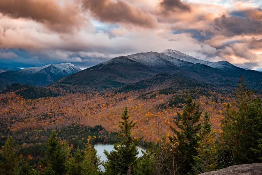 A view of a mountain range covered in snow at the top and fall foliage at the bottom.