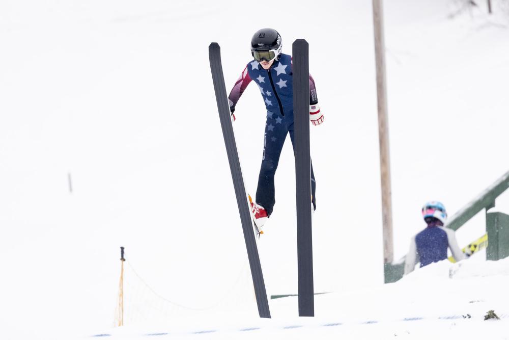 A ski jumper taking flight before a snowy sky.