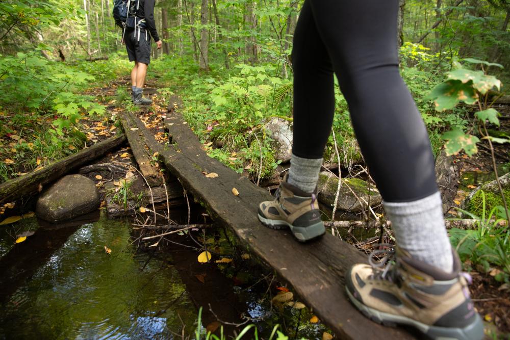 A hiker crosses a creak on a plank of wood.