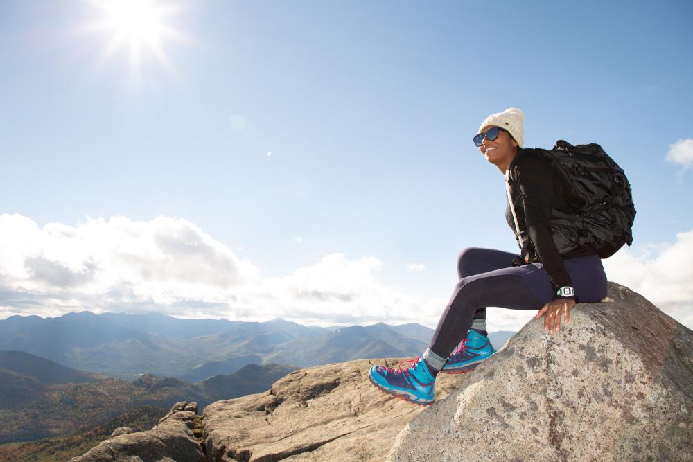 A woman sits on top of a rocky mountain, overlooking the mountain range.