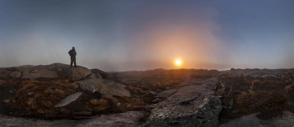 A hiker standing on a mountain summit during a foggy sunrise.