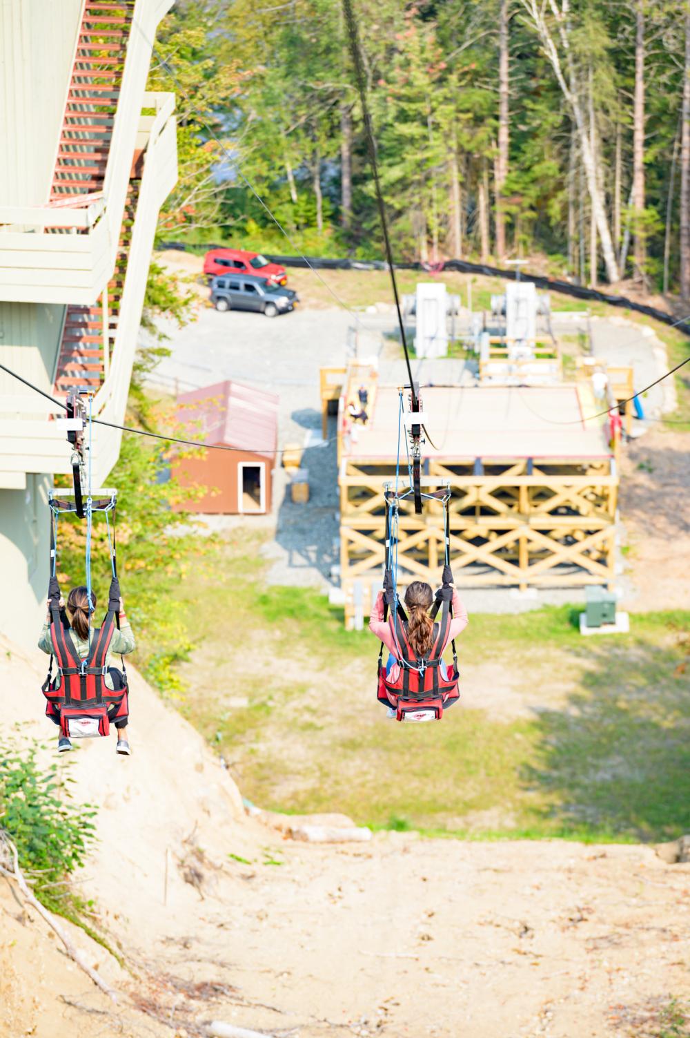 two women ride a zipline down to a platform.