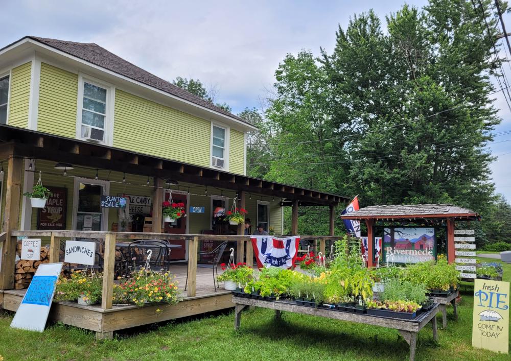 Rivermede Farm Market is a yellow building with a big front porch. Two men and their dog are on the front porch