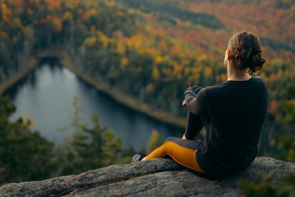 A woman sits on a rock overlooking fall foliage mountain views.