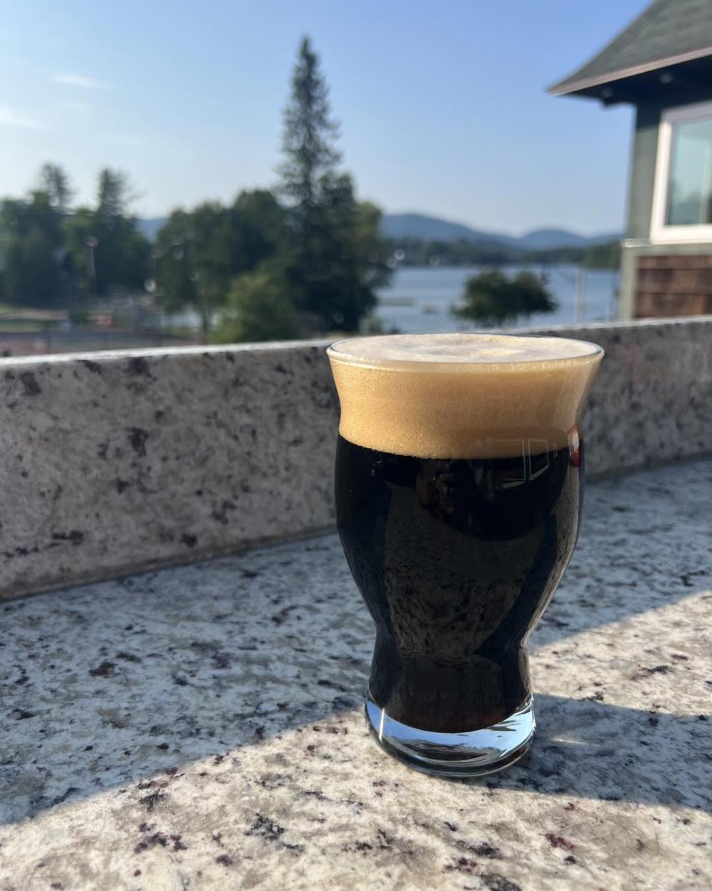 A dark glass of beer with a thick head of foam sits on a stone outdoor bar.