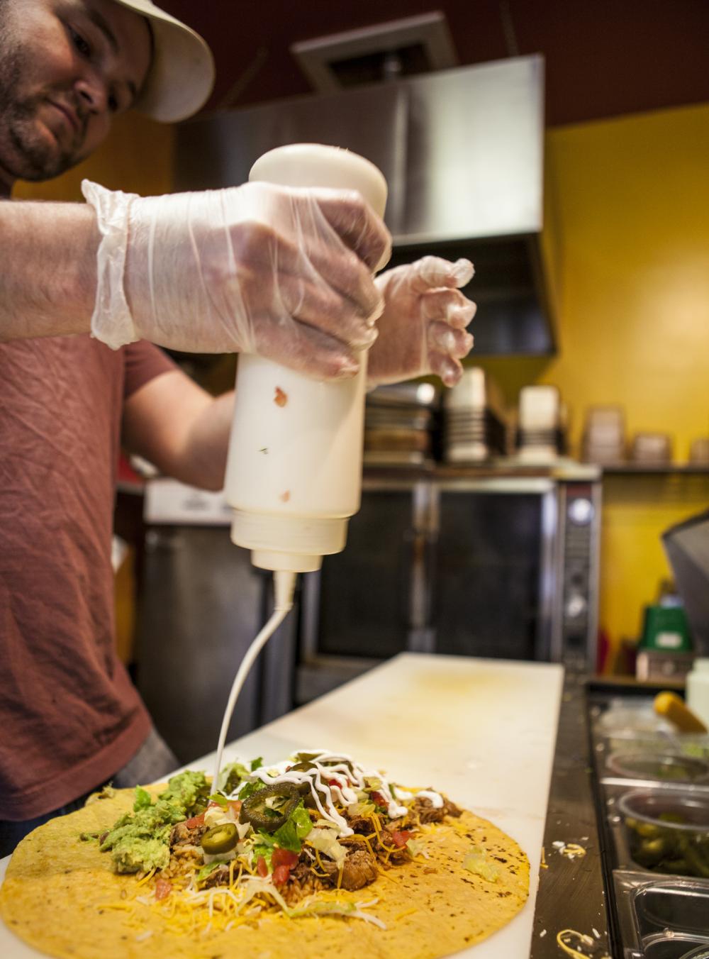 A man pours sour cream on a burrito.